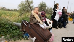 غزہ سے مصر جانے والے ایک پناہ گزین فلسطینی خاندان کی بچی سوٹ کیس پر بیٹھی ہے۔ 